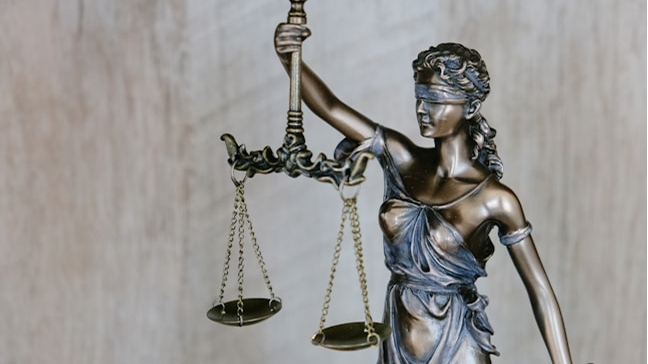 A bronze statue of Lady Justice, blindfolded and draped in flowing robes, holds up a set of scales against a light wooden background.