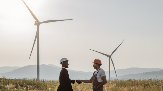 Two men shaking hands with two windmills in the background